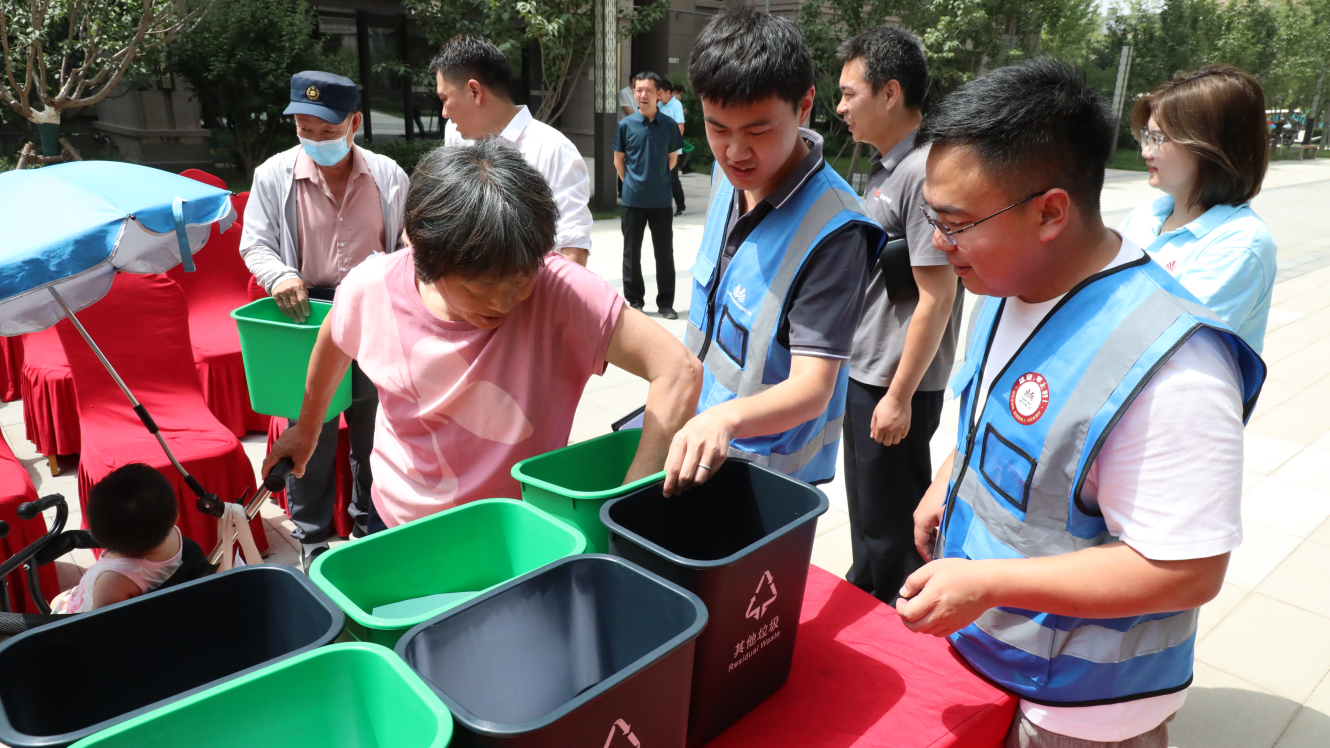 “垃圾分類志愿服務隊”隊員向居民發放垃圾桶。生態建設公司供圖